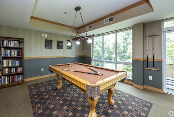 A pool table in a room with a bookshelf and a window.