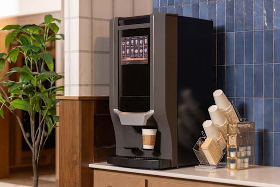 A black coffee machine on a counter with a plant to the left.