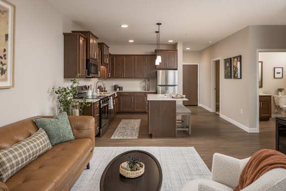 A brown leather couch with a green pillow is in the foreground of a modern kitchen and living room.