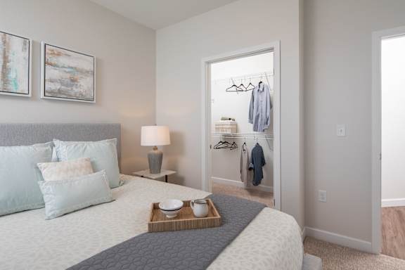 A bedroom with a bed, nightstand, lamp, and a closet with clothes hanging.