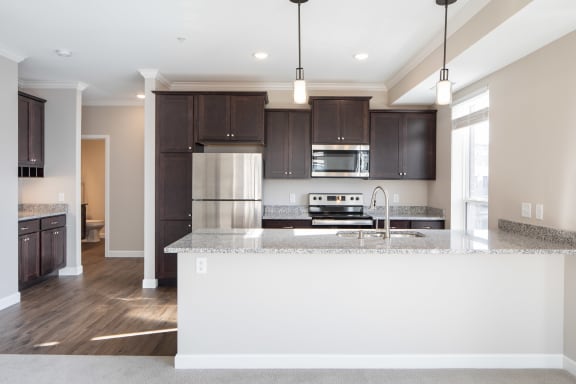 a kitchen with dark wood cabinets and a large island with granite countertopsat The Carver Apartments, Chaska, MN 55318