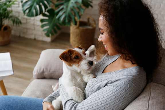 A woman is sitting on a couch holding a small dog.