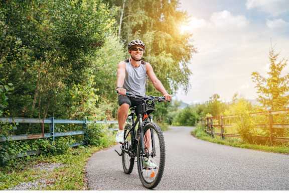 A man is riding a bicycle on a paved path in a wooded area.