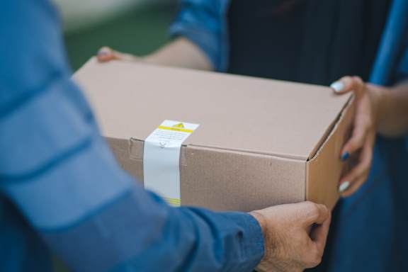 A person is holding a cardboard box with a white label on it.