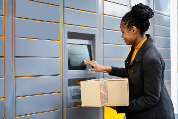 a woman holding a box in front of an automated teller machine