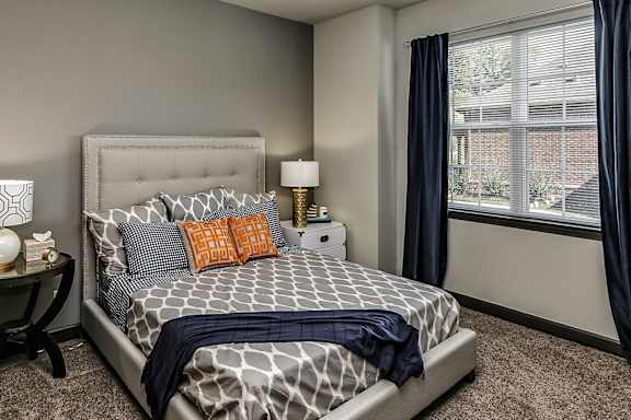 A carpeted bedroom with a bed, nightstand, and window.