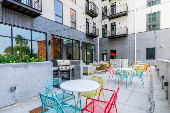 A patio with tables and chairs is surrounded by buildings.