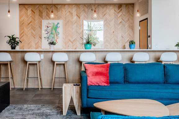 A blue couch with a red pillow sits in front of a bar with white stools.