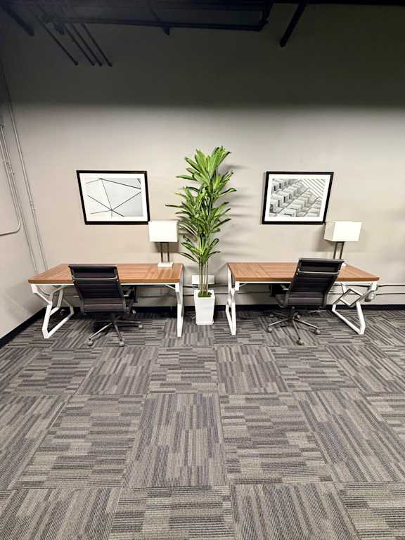A room with a grey carpet and a wooden table with two chairs.