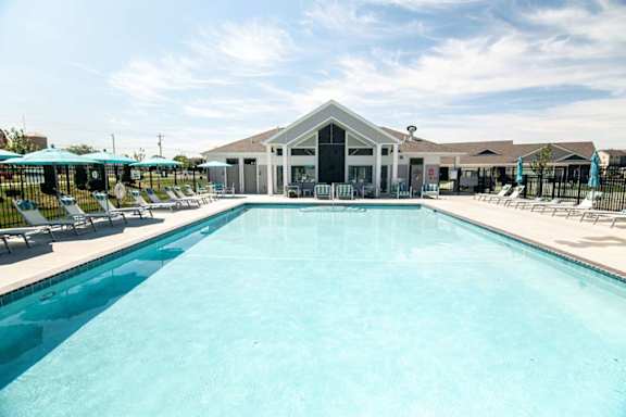 A large swimming pool in front of a building with a black fence and blue umbrellas.