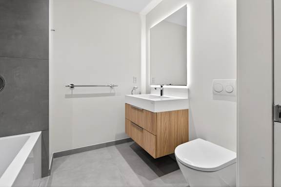A modern bathroom with a white sink and a wooden cabinet.