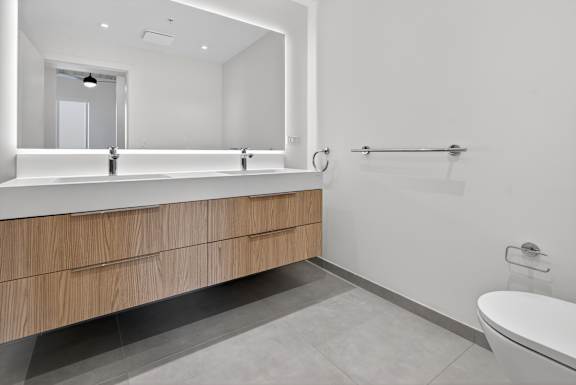 A modern bathroom with a large mirror, a sink with a vanity, and a toilet.