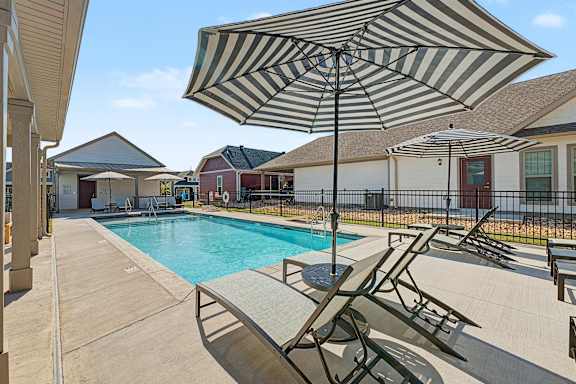 A striped umbrella is over a lounge chair by a pool.