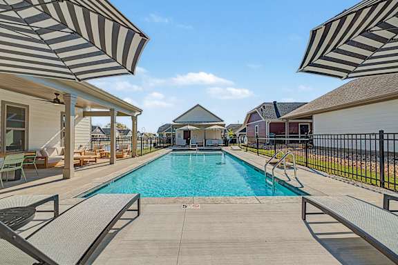 A pool surrounded by a black fence and striped umbrellas.