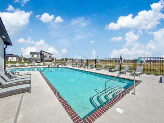 A large swimming pool with lounge chairs and a fence in the background.