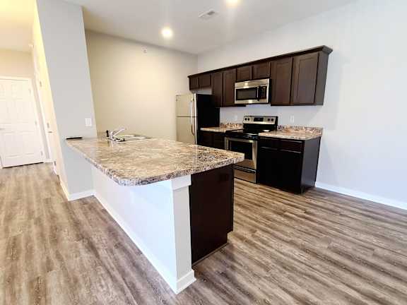 A kitchen with a granite countertop and dark brown cabinets.