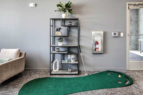 A grey shelf with various decorative items stands in a room with a green rug on the floor.