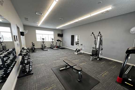 A gym with a variety of equipment including dumbbells, weight machines, and a bench press.
