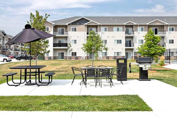 A black umbrella is on a picnic table in front of apartment buildings.