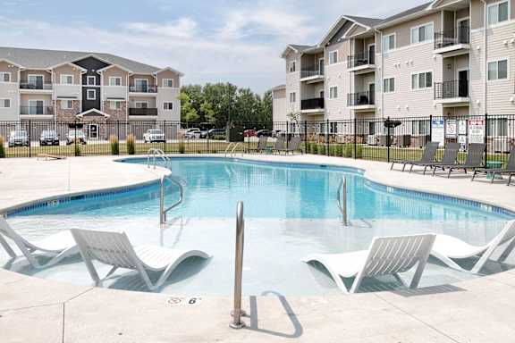 A swimming pool with lounge chairs and apartment buildings in the background.