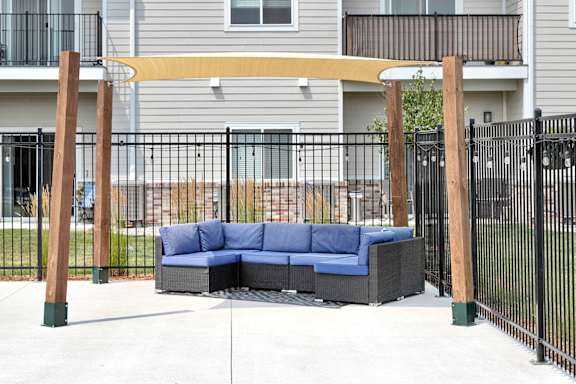 A blue couch is placed on a patio with a black fence.
