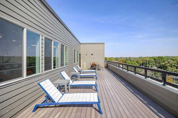 A wooden deck with blue and white chairs and a railing.