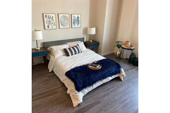 A bed with a blue blanket and a bottle of perfume on it.