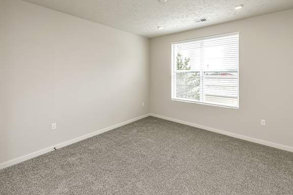 A room with a carpeted floor and a window with blinds.
