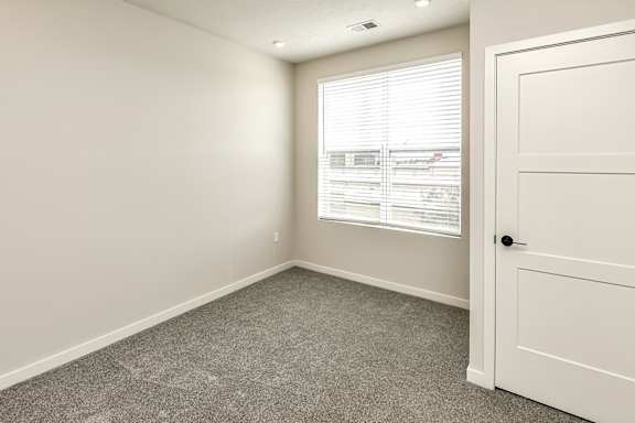 A room with a carpeted floor, a window with blinds, and a white door.