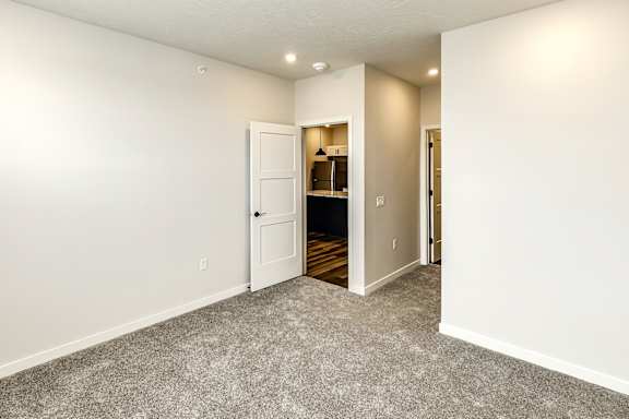 A room with a carpeted floor and a white door leading to a kitchen.