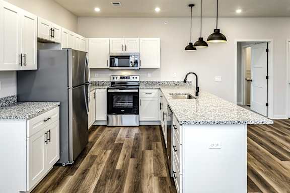 A kitchen with a refrigerator, microwave, oven, and sink.