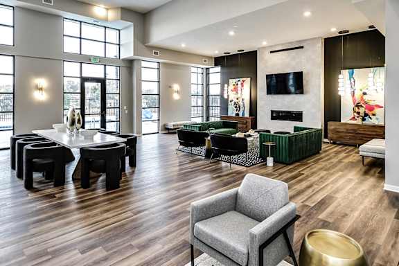 A grey chair is in the foreground of a spacious room with wooden floors and a variety of seating options.