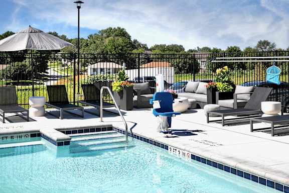 A pool with a blue chair and a black umbrella.