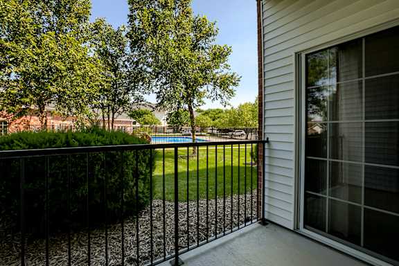 A black metal fence surrounds a patio with a view of a green lawn and trees.