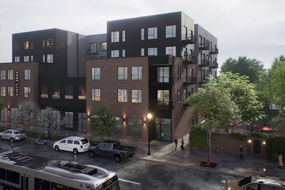 A modern building with a black and brown facade is surrounded by trees and vehicles.