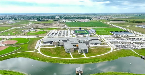 An aerial view of a large building complex with a parking lot and a body of water in the foreground.