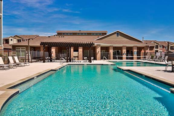 A large swimming pool in front of a building with a covered patio area.