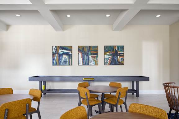 A room with a long table and chairs and three paintings on the wall.