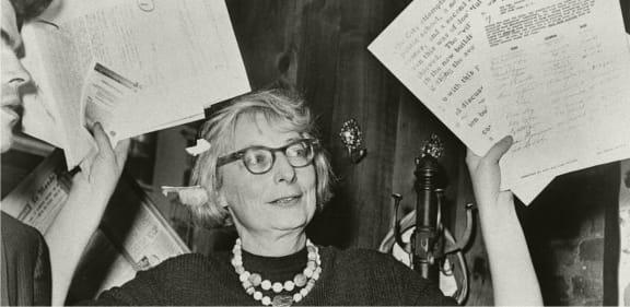 A woman with glasses and a pearl necklace is surrounded by papers. at The Lady, South Carolina