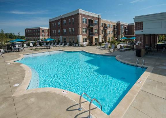 A large swimming pool surrounded by a patio area with chairs and umbrellas.