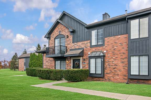 A red brick house with a balcony and a green lawn in front.