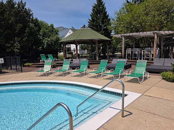 A pool with a metal ladder and a gazebo in the background.