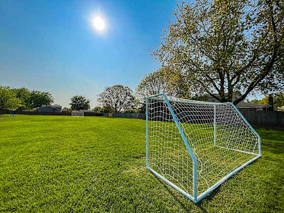 A soccer goal stands on a lush green field under a clear blue sky.