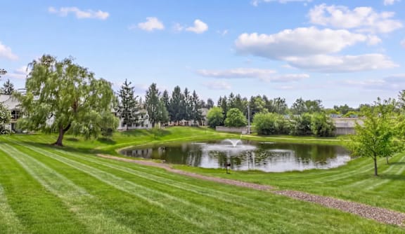 A serene park with a pond and a fountain in the middle.
