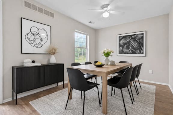 A dining room with a table, chairs, and two framed pictures on the wall.