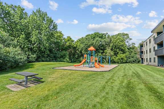 A playground with a slide and picnic table in a grassy area.