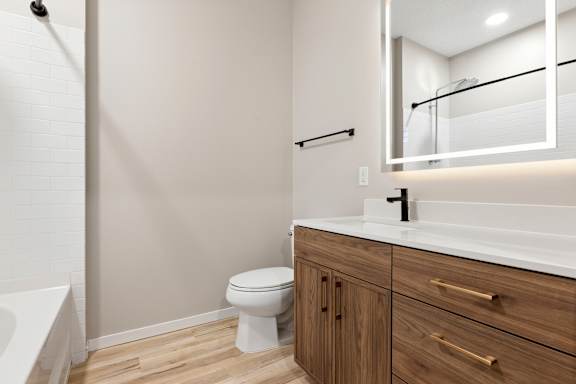 A white toilet sits in a bathroom with a white tub and a white sink.