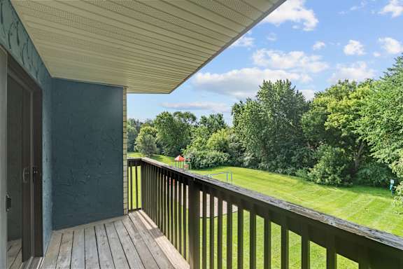A balcony with a view of a green lawn and trees.