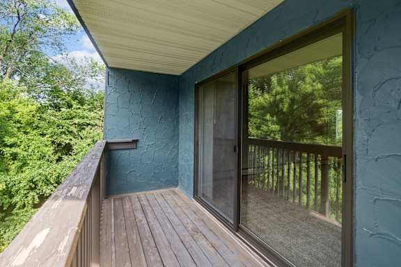 A balcony with a glass door and a window overlooking a forest.