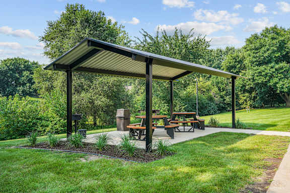 A picnic area with a shelter and benches is surrounded by greenery.